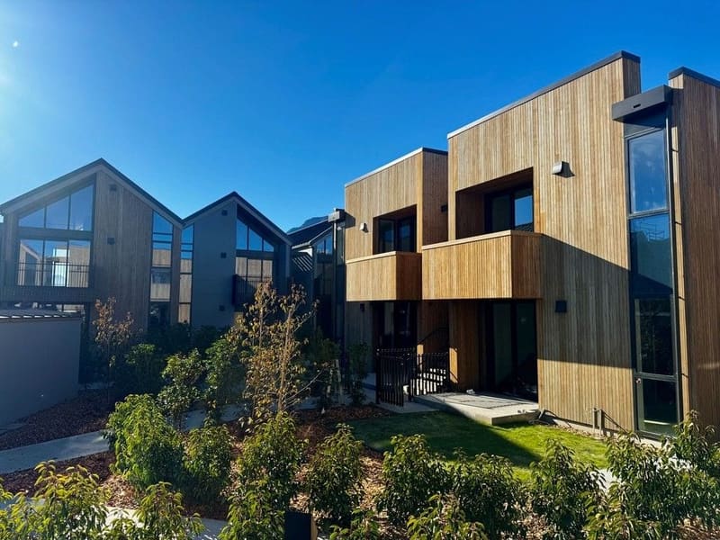 Black balustrades on cedar townhouses above a planted garden, Arthurs Point