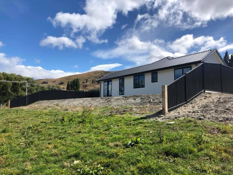 Dark colour steel panel fencing along a driveway with Queenstown mountains behind