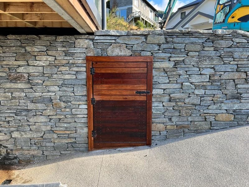 Horizontal timber pedestrian gate set into a schist stone wall, Queenstown