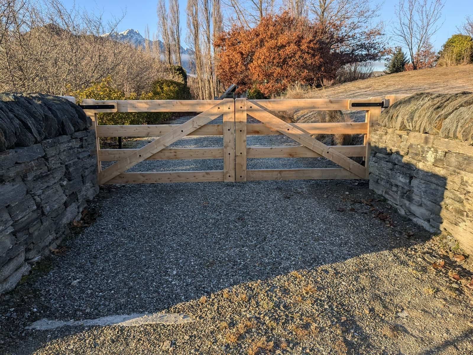 Macrocarpa timber gate set into schist stone walls with The Remarkables behind, Central Otago