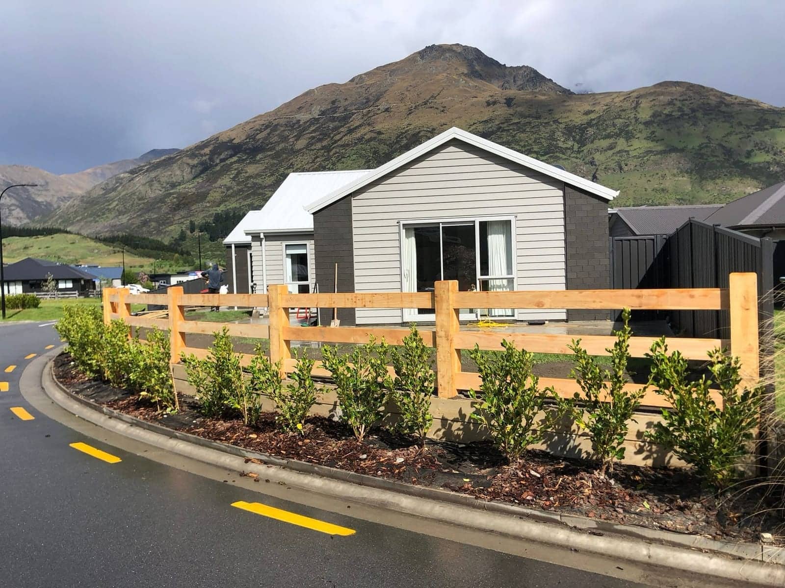 Macrocarpa post and rail fence along a street with mountain backdrop, Queenstown