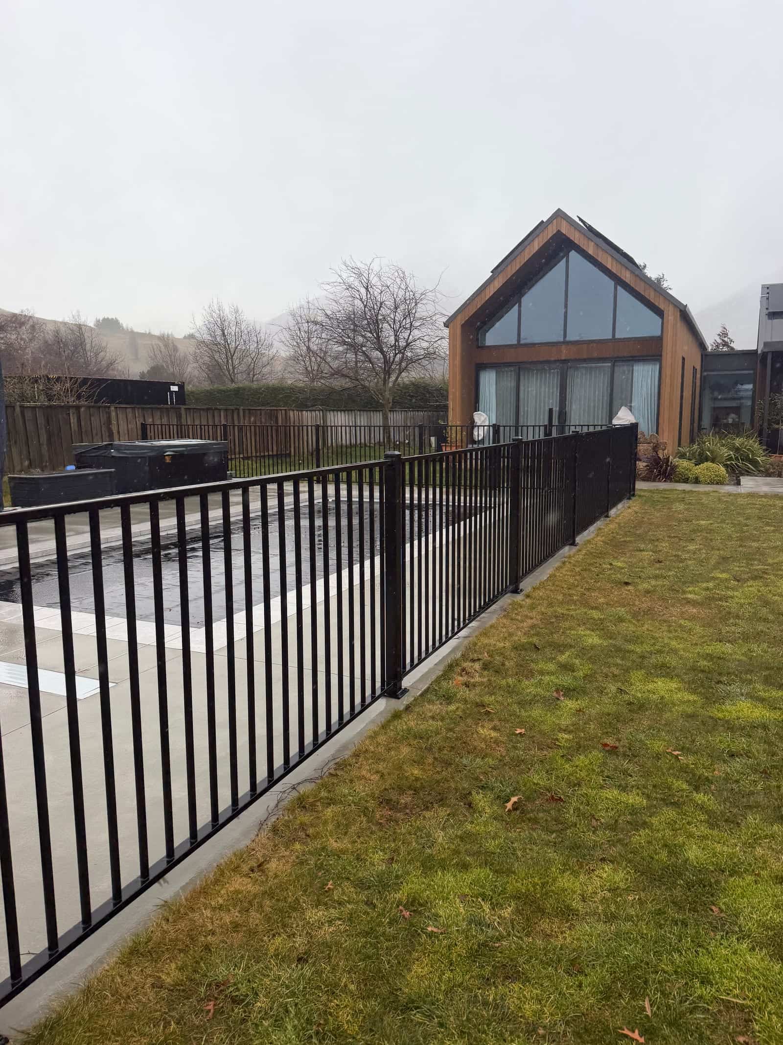 Black tubular steel pool fence beside a modern cedar-clad home, Queenstown