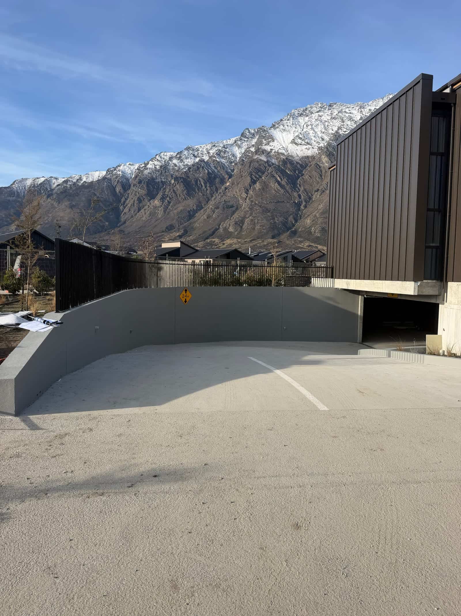 Black slat fencing above a commercial retaining wall with The Remarkables behind, Queenstown