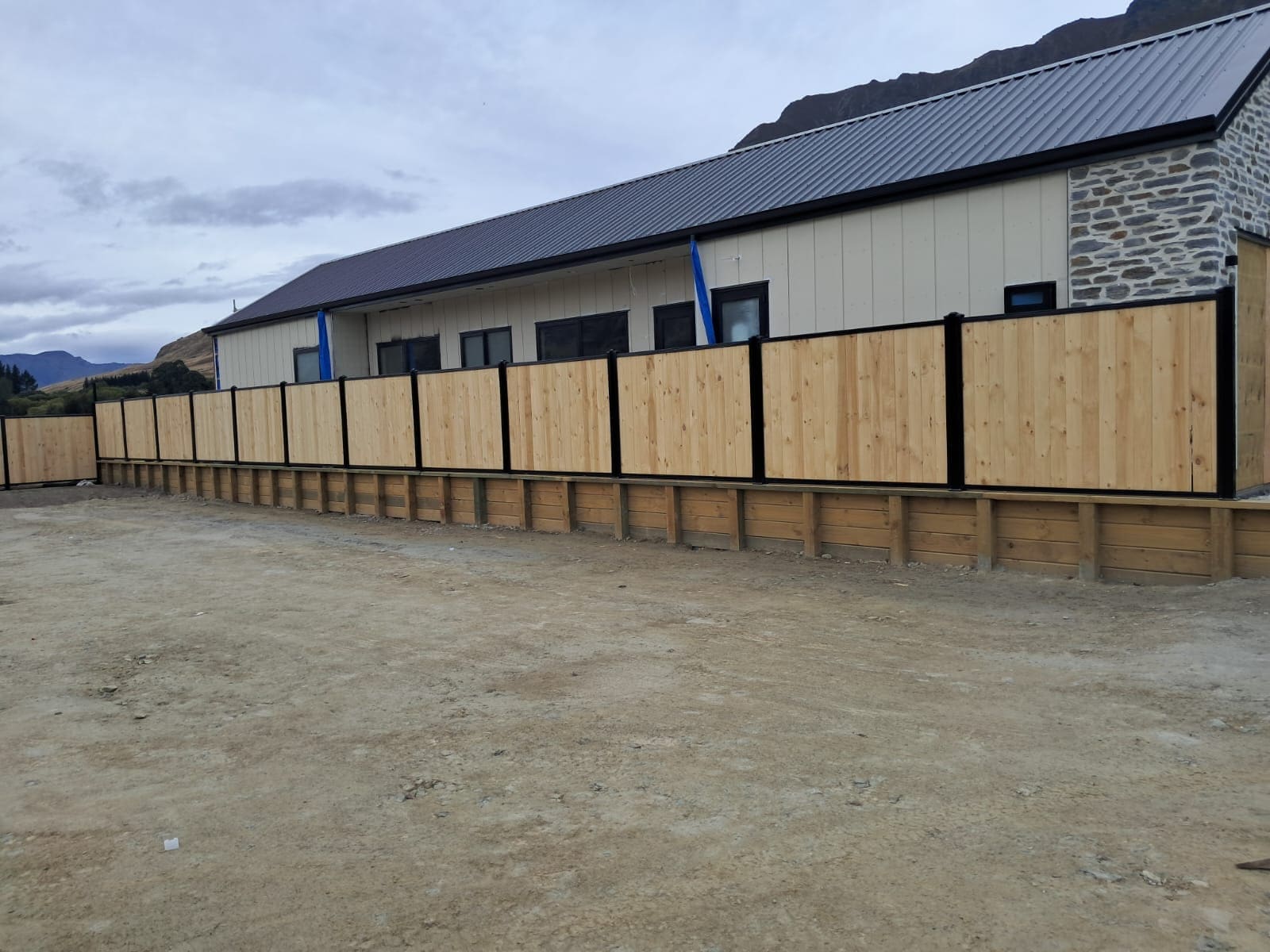 Smart wall fencing with laminated timber palings in a black aluminium frame above a timber retaining wall, Queenstown